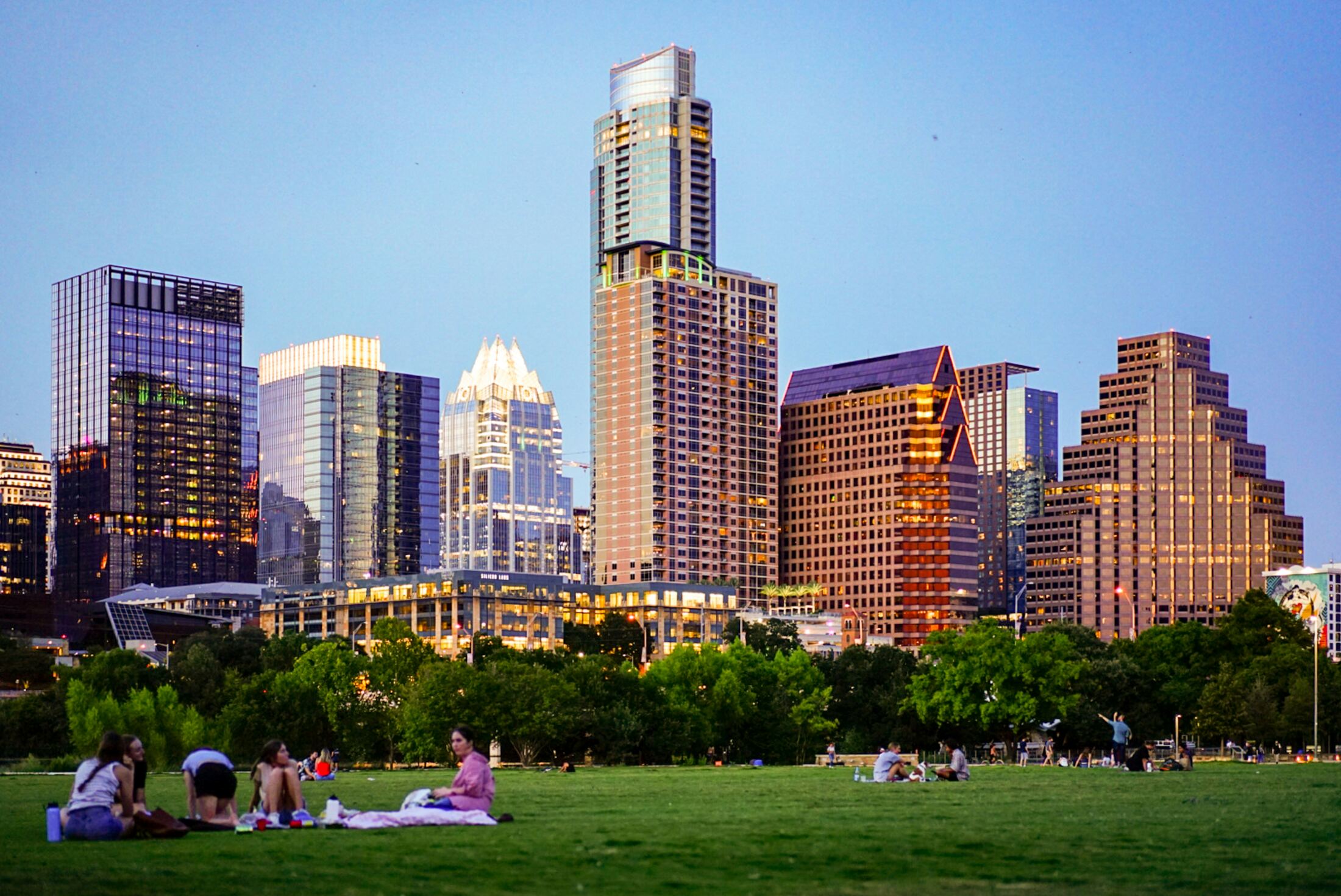 Picnic blankets on the park lawn below the downtown Austin skyline at dusk